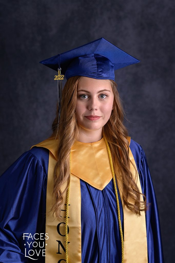 Studio cap and gown portrait, photographed in the Faces You Love studio in Kansas City. Senior girl is wearing a royal blue cap and gown, with gold stole and sash.