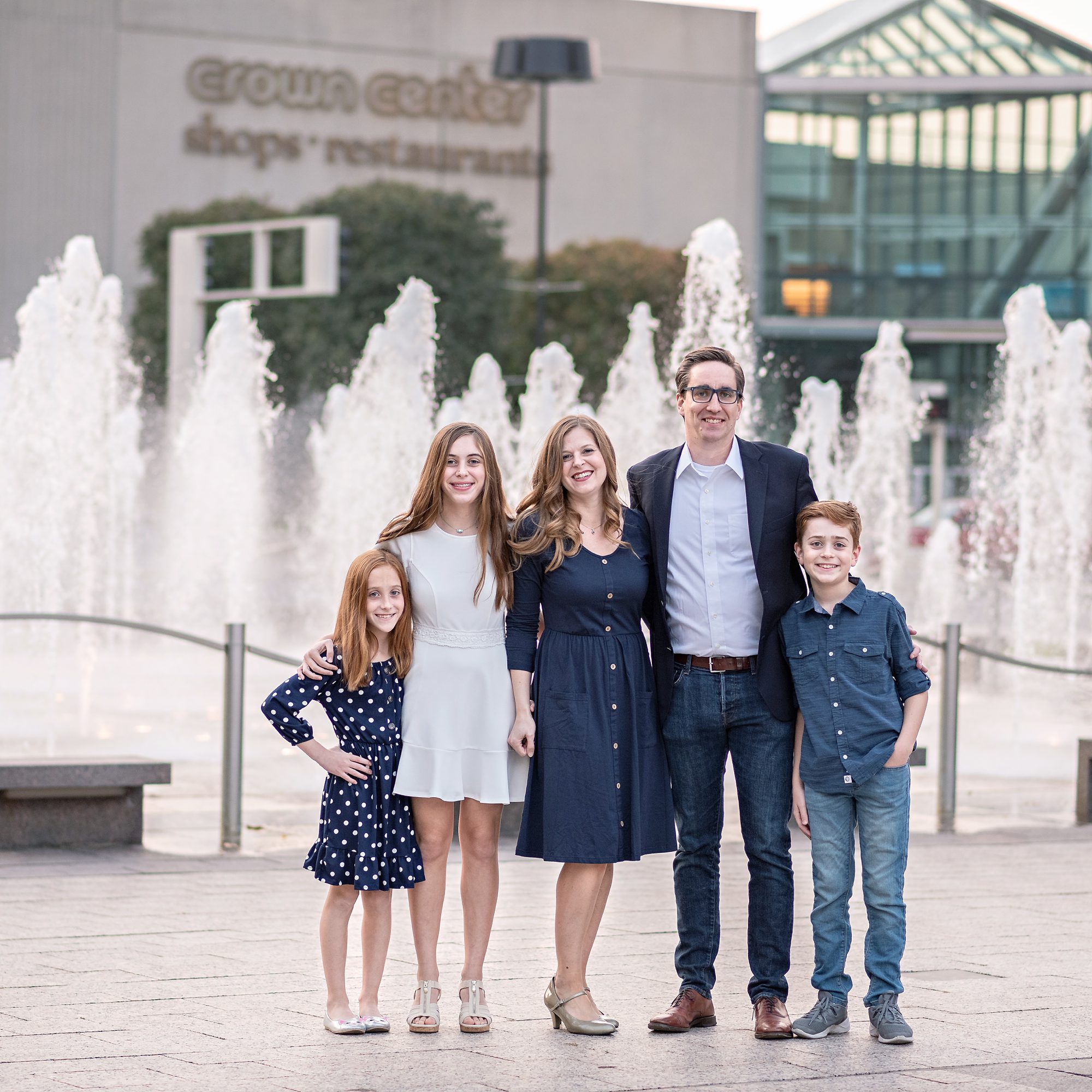 Family photo taken in downtown Kansas City, near Crown Center. Family is dressed in blues and standing in front of fountains. Photographed by Faces You Love Photography.