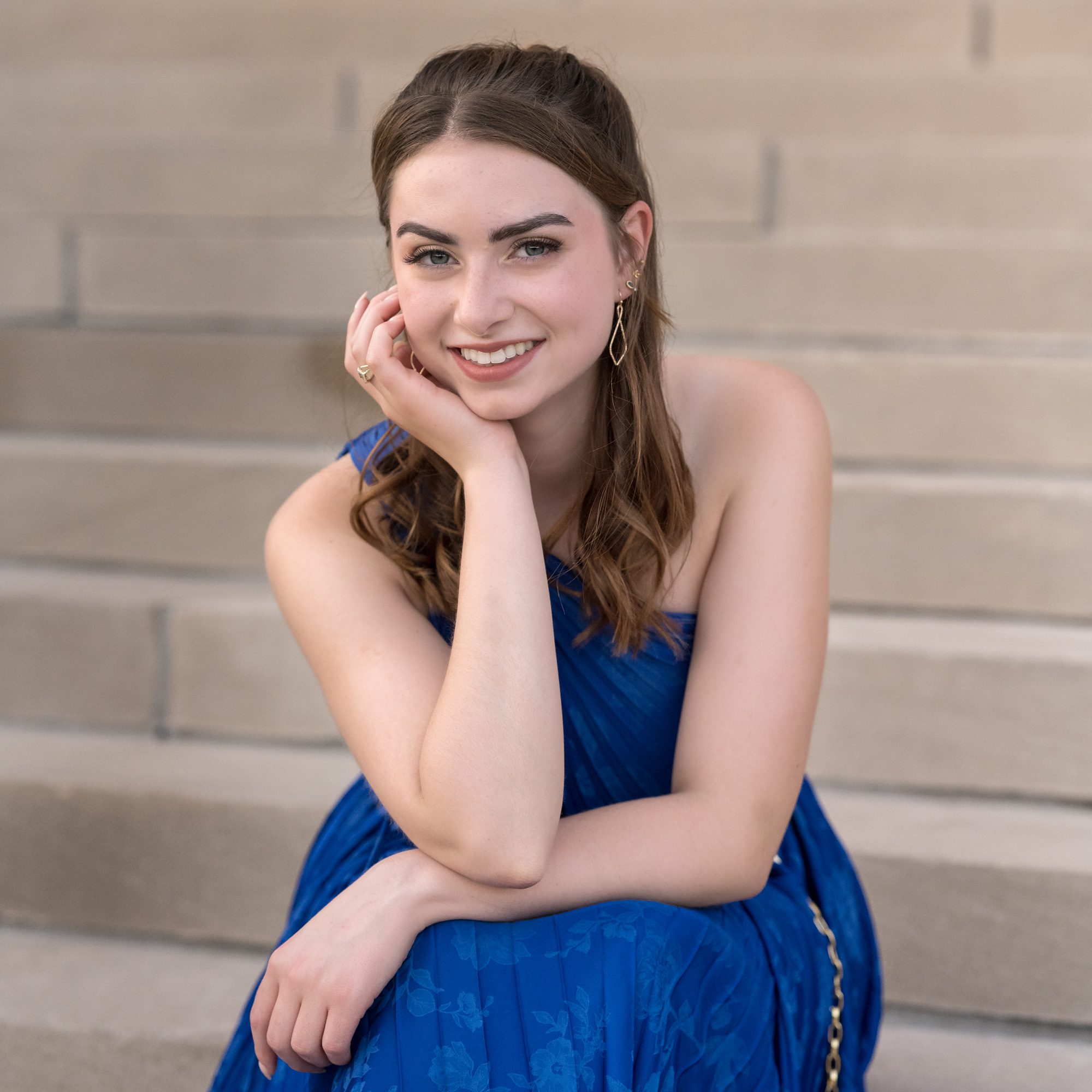High School Senior Portrait photographed by Faces You Love, at the Nelson Atkins Art museum in Kansas City. Senior girl is wearing a royal blue dress, while sitting on the steps.