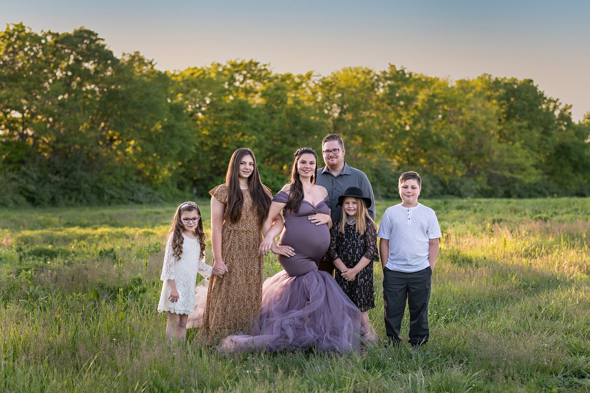 Outdoor family portrait, with 4 children and expectant mother. Mom is in an elegant maternity gown from the photography studio's dress collection. Photographed in Kansas City by Faces You Love.