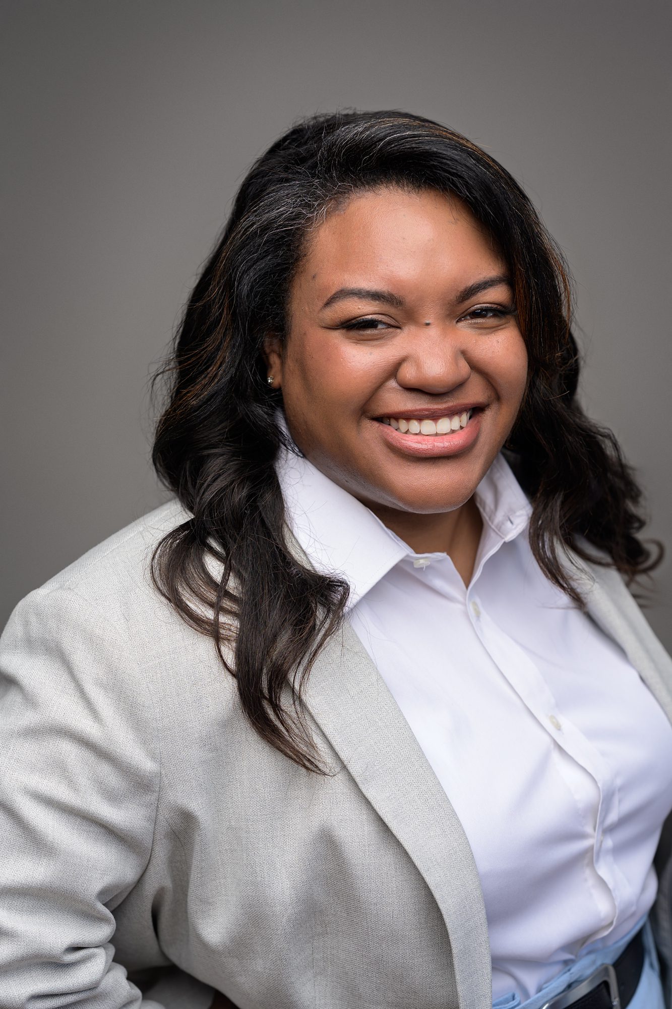 Smiling, professional African American woman headshot, photographed in Overland Park by Faces You Love. She's wearing a white button down, and has an oatmeal color blazer on.